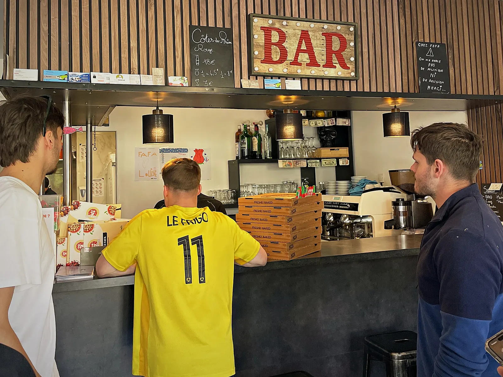 Des clients accoudés au comptoir de Pizza Sympa, sous l’enseigne « BAR »