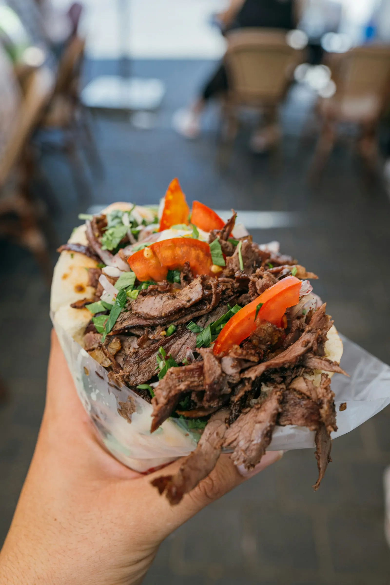 Une pita garnie de viande grillée, de tomates et d’herbes, tenue à la main